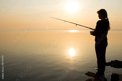 silhouette of a young girl fishing at sunset near the sea