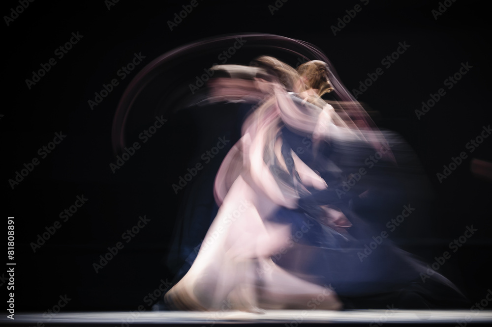 Fototapeta premium Blurry dancers in dynamic dance. Dancers dance on the dark stage. Slow shutter speed photography. .
