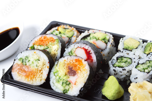 Assorted sushi rolls in a black plastic tray against white backg