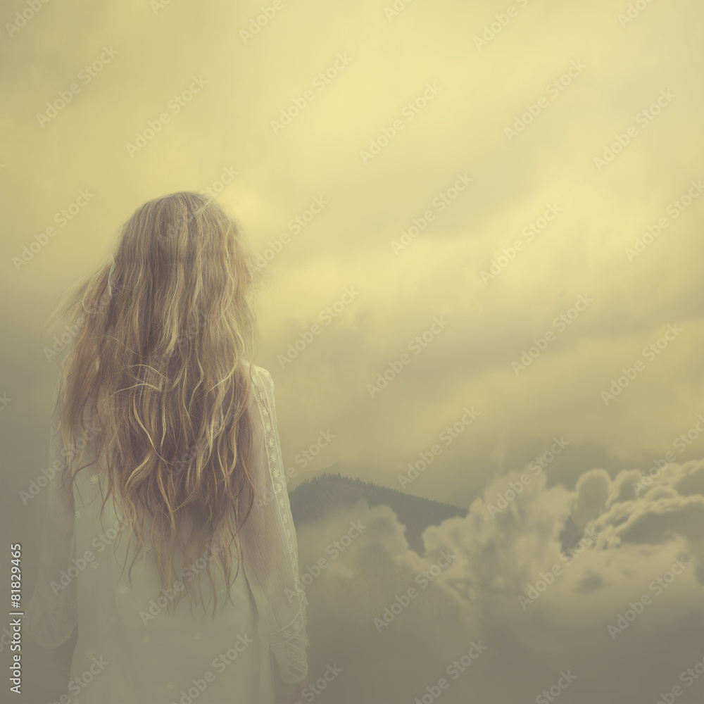 Fototapeta premium girl in a dress stands in the clouds over the mountains