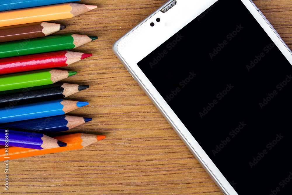 Naklejka premium pencils color and smart phone on wood background, top view