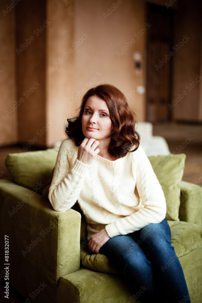 Portrait of mid-adult woman looking at camera sitting in armchair in bright living room Portrait of mid-adult woman looking at camera sitting in armchair in bright living room