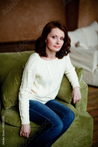 Obraz na płótnie Portrait of mid-adult woman looking at camera sitting in armchair in bright livi