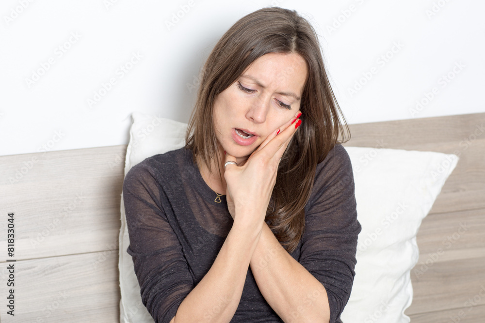 Mid-adult woman sitting in bed with toothache