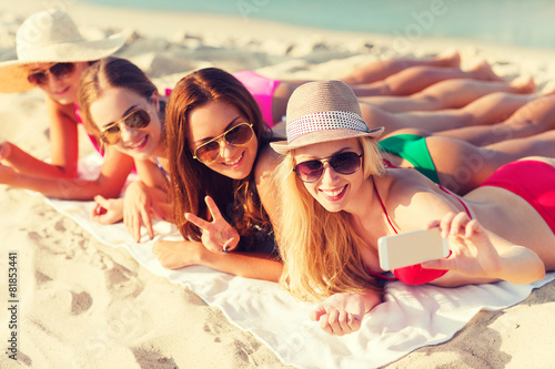 group of smiling women with smartphone on beach