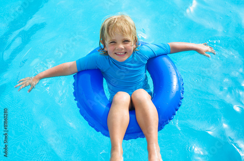 Happy little boy  with blue life ring in the swimming pool