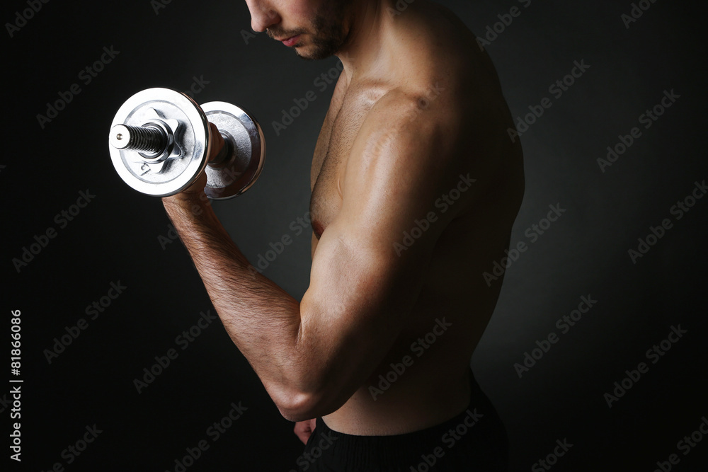 Muscle young man holding dumbbell on dark background Muscle young man holding dumbbell on dark background