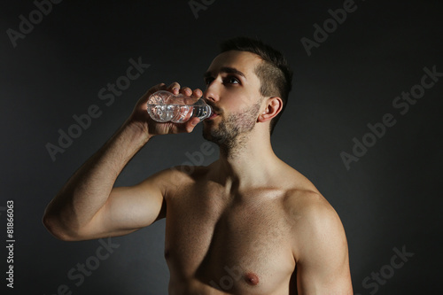 Muscle young man holding bottle of water on black background