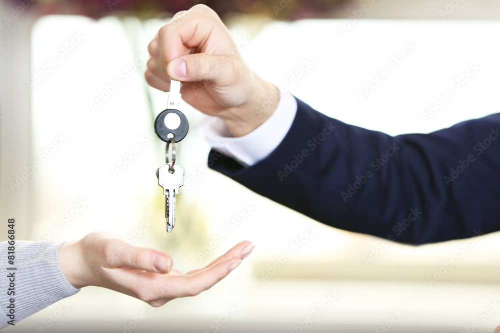 Hand of businessman giving keys to female hand on blurred background Hand of businessman giving keys to female hand on blurred background