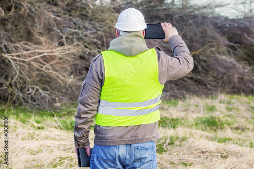 Forest engineer with tablet PC near pile of twigs
