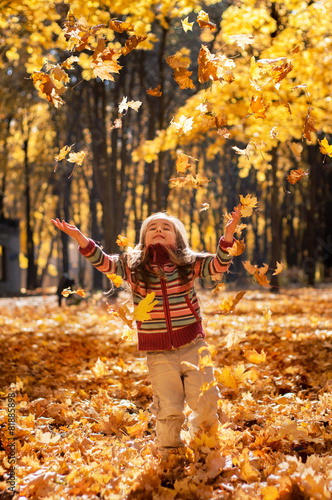 Little happy girl throws up fallen leaves