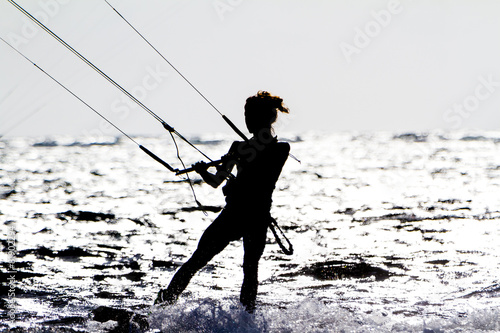 A young woman kite-surfer rides against the sun