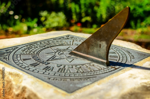 A brass sundial mounted on a stone plinth photo