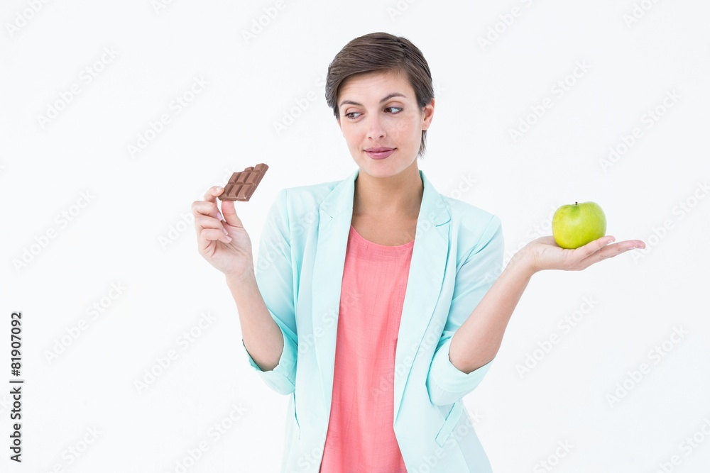 Brunette choosing between an apple and chocolate bar Brunette choosing between an apple and chocolate bar