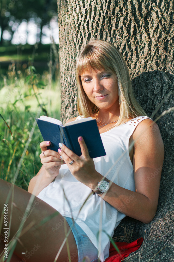 Fototapeta premium young woman sitting in the park and reading a book