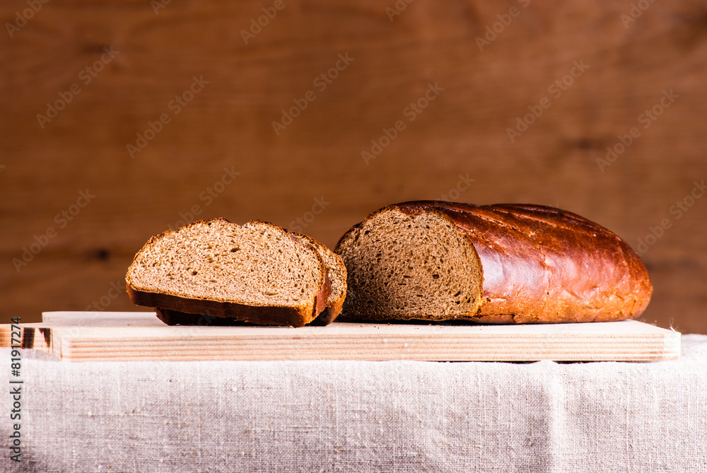 Cut loaf of fresh bread on burlap on wooden table