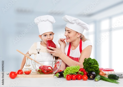Adorable. Mother feeding kid daughter vegetables in kitchen