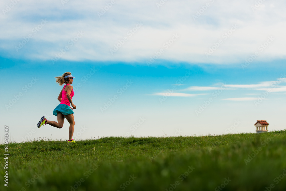 Blonde girl athlete runs in a green meadow in the hills