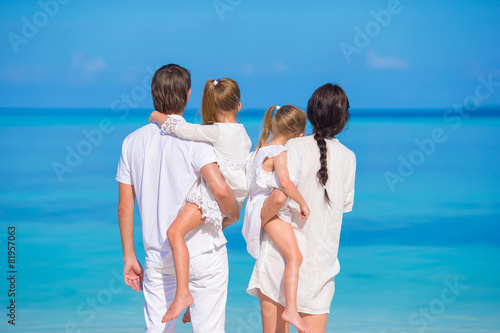 Back view of young family of four on white beach during summer