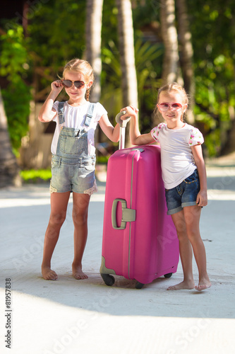 Little adorable girls with big suitcase on tropical white beach