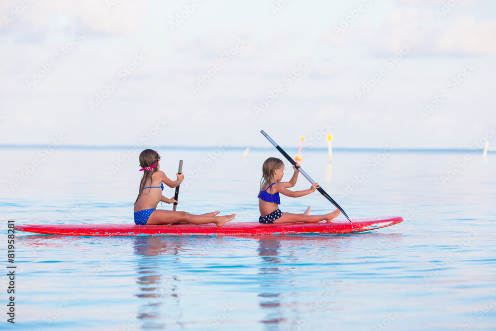 Little girls swimming on surfboard during summer vacation