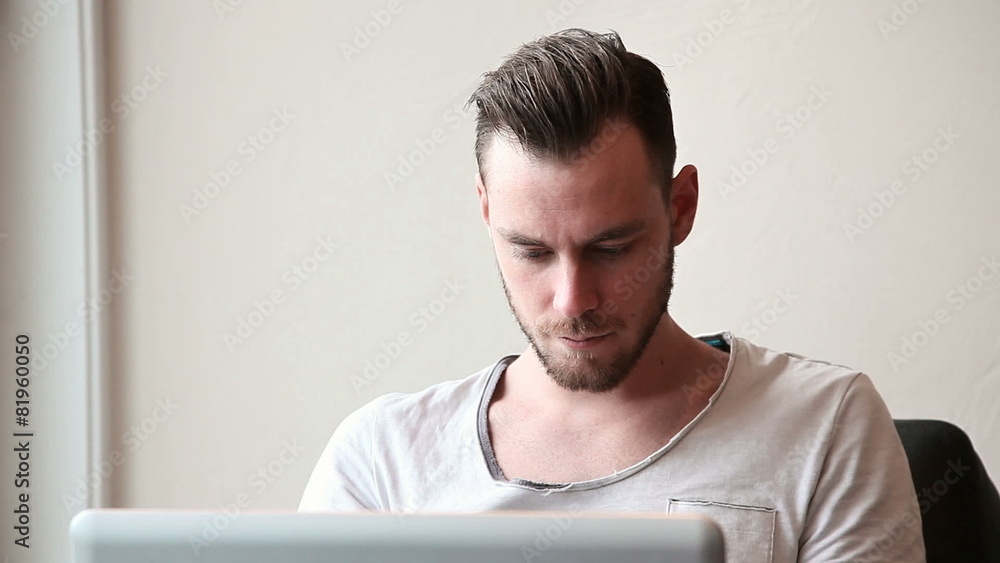 A young man with a laptop sitting down inside A young man with a laptop sitting down inside