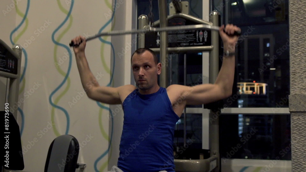 Young man exercising on lat machine in gym at night Young man exercising on lat machine in gym at night