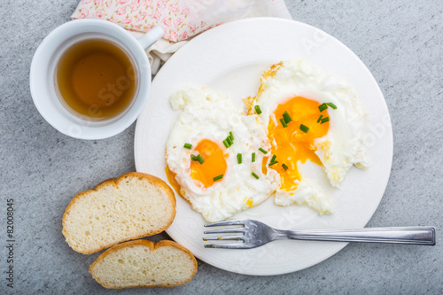 Two fried eggs with chives on white plate