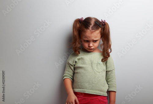 Unhappy abandoned kid girl looking down on blue background