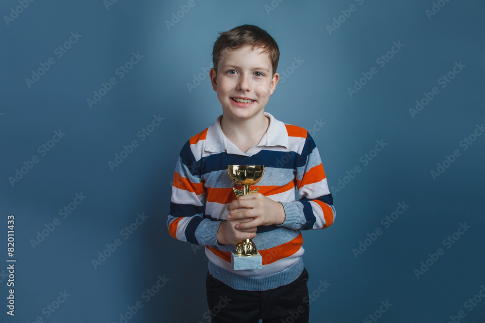 European-looking boy of ten years holding a cup award on a gray European-looking boy of ten years holding a cup award on a gray