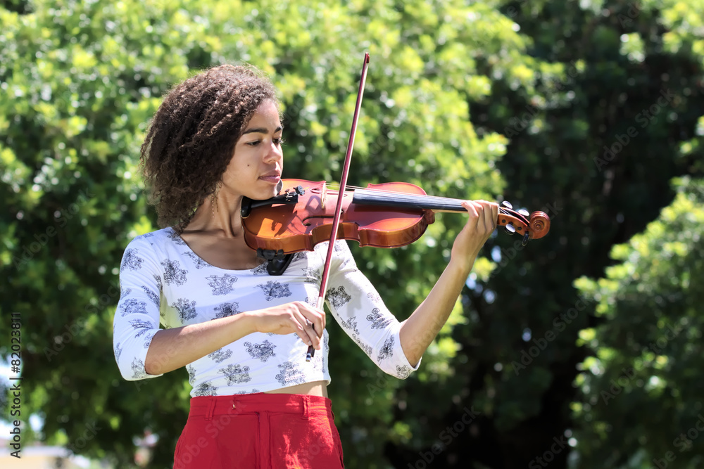 Young woman with curly hair playing violin outdoors
