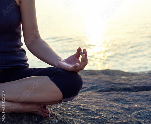 The woman meditating in a yoga pose on the tropical beach.