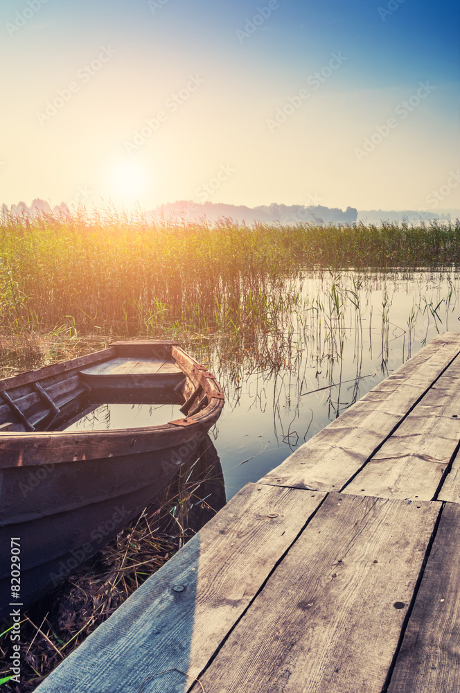 Old boat on the coast of lake at sunset - obrazy, fototapety, plakaty 