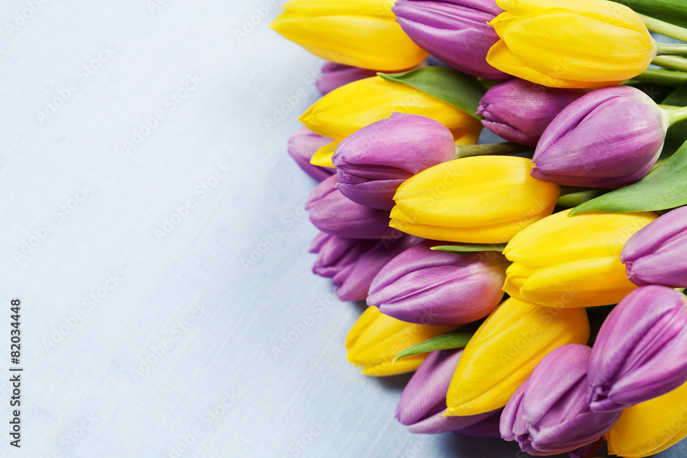 Obraz premium Bouquet of beautiful purple and yellow tulips on blue background