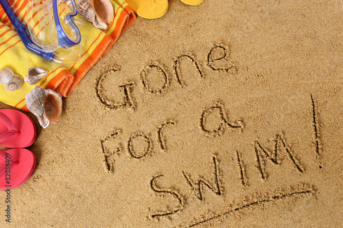Gone for a swim word text message written in sand on a tropical beach with seashells and accessories summer holiday vacation photo