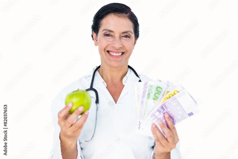 Confident female doctor holding green apple and banknotes Confident female doctor holding green apple and banknotes