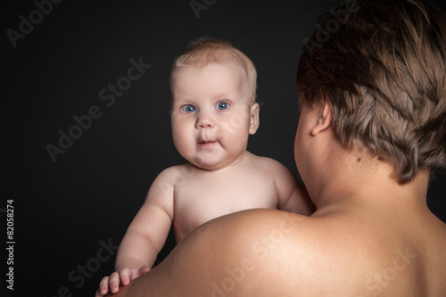 Cute baby looking over father's shoulder .