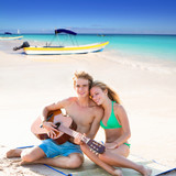 Blond tourist couple playing guitar at beach