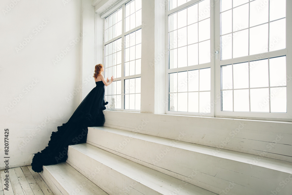 Fashion woman in black dress near big window