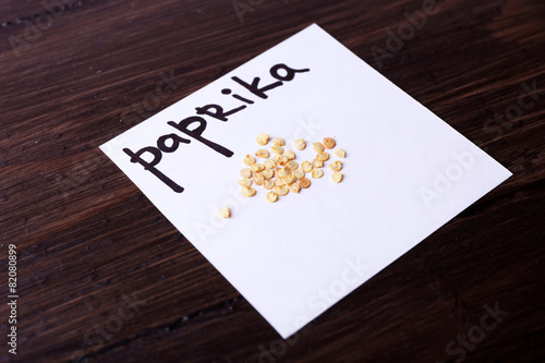 Paprika seeds on piece of paper on wooden background