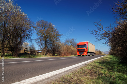 Road between flowering trees in early spring. Truck on the road.