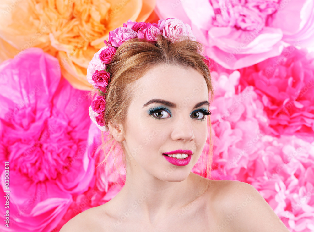 Portrait of young woman with flowers in hair on bright pink background