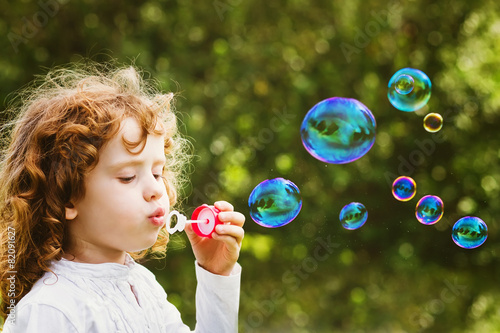 A little girl blowing soap bubbles, closeup portrait beautiful c