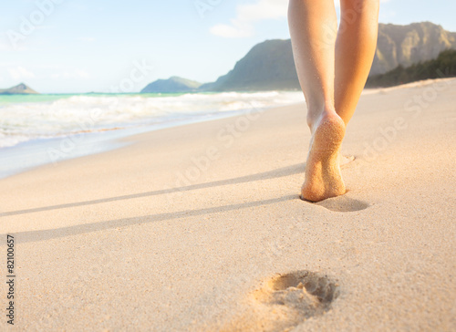 Woman walking on sandy beach leaving footprints in the sand.