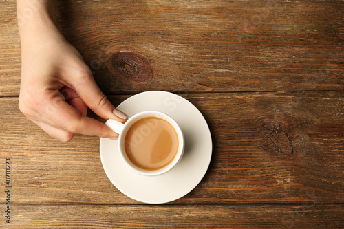 Female hand holding cup of coffee on wooden background
