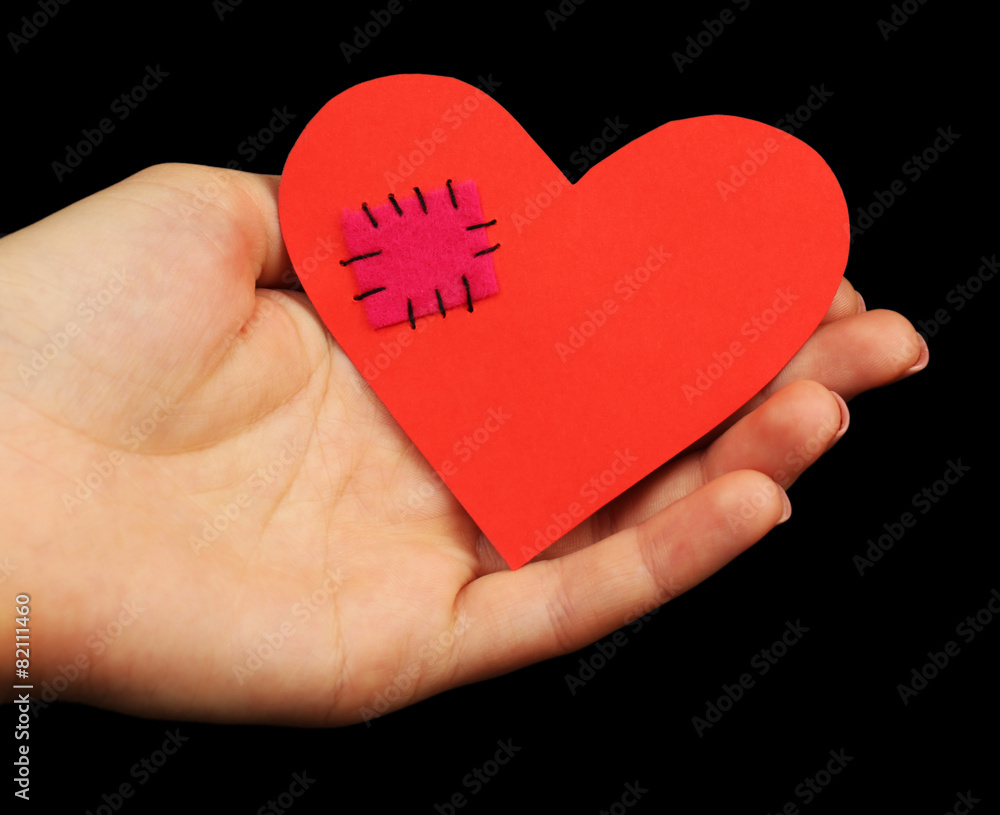 Female hand holding broken heart with patch on black background Female hand holding broken heart with patch on black background