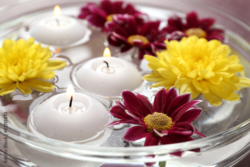 Bowl of spa water with flowers and candles, closeup