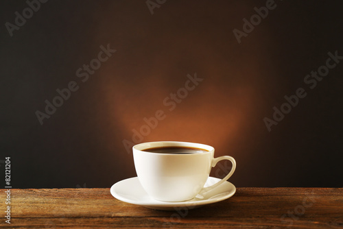 Cup of coffee on wooden table on dark background