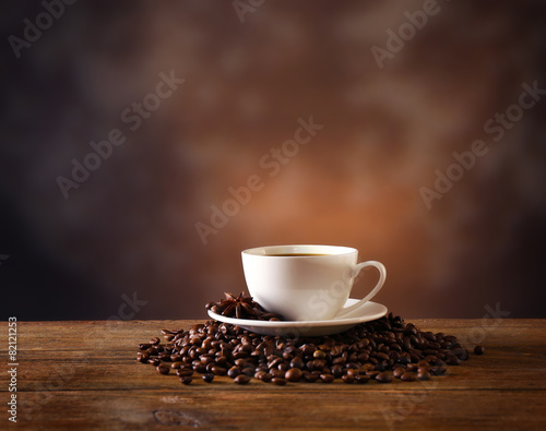 Cup of coffee with grains on wooden table on dark background