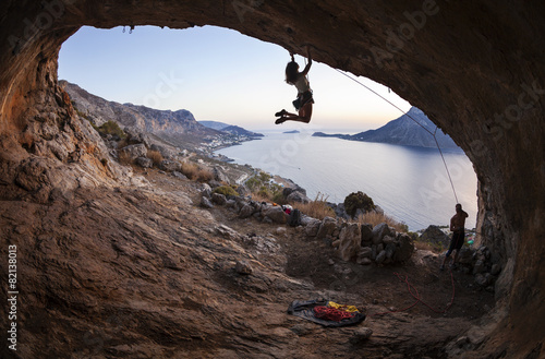 Young woman lead climbing in cave with beautiful view in background